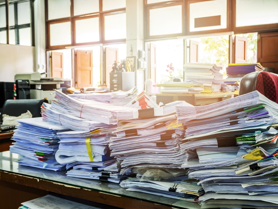 Close-up of stacks of documents in an office with sunlight shining through window in background